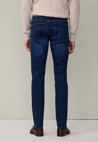 Mørkeblå denim jeans med slim fit, der har to baglommer og kontrastsyninger. Båret med en lys beige ribbet sweater og brune sko.