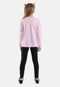 Langärmliges pinkes Shirt und schwarze Leggings mit schlichtem Design und weichem Material. Ein pinkes Haarband mit Katzenohren verleiht einen verspielten Akzent.