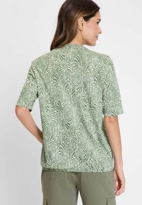 Kurzärmliges grünes T-Shirt mit einem weißen Zebramuster. Hergestellt aus weichem Material mit lässiger Passform und Rundhalsausschnitt.