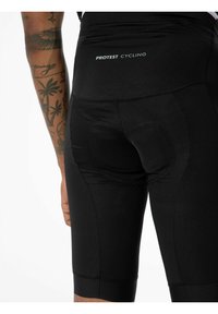 Schwarze Radhosen aus elastischem Material, ausgestattet mit einem gepolsterten Bereich für mehr Komfort, strukturierten Mustern und einem aufgedruckten Logo auf der Rückseite.