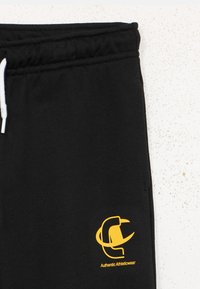 Μαύρο παντελόνι φόρμας με κορδόνι στη μέση, με κίτρινο λογότυπο και κείμενο "Authentic Athleticwear" στην αριστερή πλευρά. Μαλακή υφή υφάσματος.