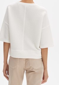 Suéter blanco texturizado de manga corta, con un diseño acanalado y un corte relajado, combinado con pantalones ligeros color beige claro con bolsillos traseros.