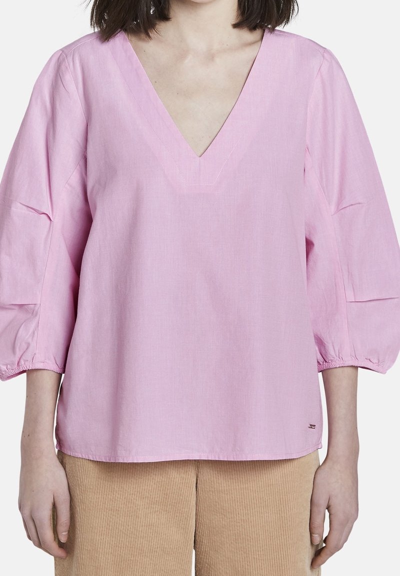 Top in cotone rosa con scollatura a V profonda, maniche a palloncino a tre quarti e dettagli di cucitura sottili. Abbinato a pantaloni in corduroy beige.