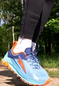 Scarpa da corsa blu chiaro con accenti arancioni, parte superiore in mesh testurizzato e lacci neri; ammortizzazione visibile, suola sagomata e forma ergonomica.