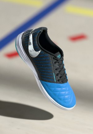 Kék és fekete sportcipő, steppelt textúrával, ezüst Nike logóval és csíkos mintával a felső részen. Fekete fűzőkkel és fehér talppal rendelkezik.