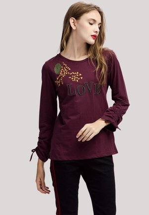 Camiseta de manga larga burdeos con la palabra "AMOR" en negro, detalles de bordado floral y fruncidos en los puños de las mangas.
