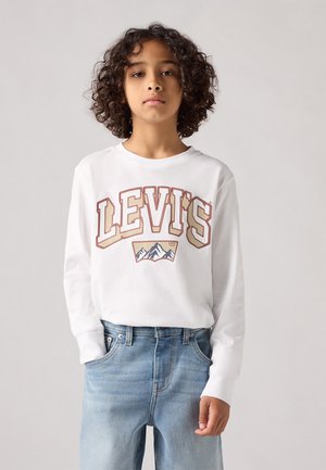 Camisa blanca de manga larga con un colorido logo de Levi's y un gráfico de montaña, combinada con jeans de mezclilla azul claro.