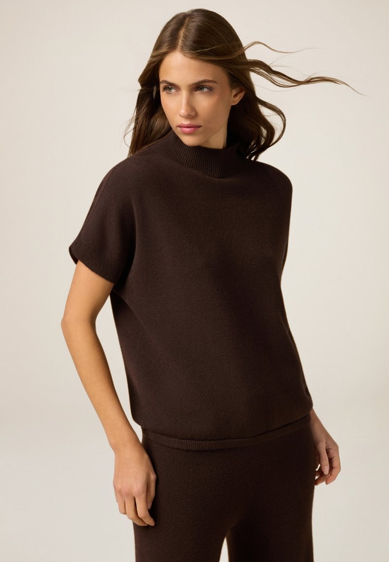 Brauner gestrickter Pullover mit hohem Kragen und kurzen Ärmeln. Texturiert, lockere Passform und kombiniert mit passenden braunen Unterteilen.