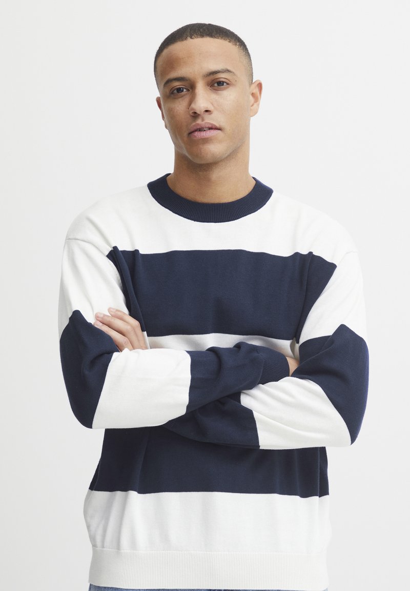 Maglione in maglia con righe orizzontali blu navy e bianche, collo tondo, polsini e orlo a costine, con un retro completamente blu navy. Texture morbida.