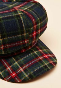 Wełniana czapka z granatowo-czerwono-zielonym wzorem w kratę, z płaskim daszkiem i zaokrąglonym wierzchołkiem, o teksturowanym wykończeniu.
