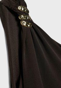 Gros plan sur un tissu noir rassemblé et maintenu par trois clips métalliques dorés, brillants et irréguliers, avec une texture martelée.