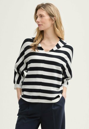 Pull en tricot à rayures noires et blanches avec un col en V, des manches trois-quarts et une coupe décontractée. Détail de couture remarquable sur le devant.
