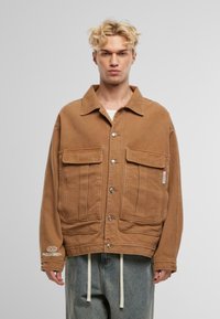 Braune Canvasjacke mit einem Kragen, zwei großen Fronttaschen und silbernen Knöpfen. Verfügt über ein Logo am Ärmel und einen entspannten Schnitt.