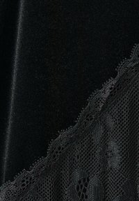 Černá látka s propracovaným květinovým krajkovým lemováním, ukazující jemnou síť a detailní stehy podél okraje.