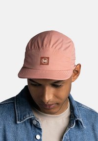 Gorra rosa con un logo redondo marrón de "Buff", hecha de un tejido ligero, que presenta un ala suave y una textura gathered en la parte superior.