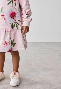Rosa Sweatshirt-Kleid mit Blumenmuster, mit Rüschensaum und langen Ärmeln. Weiße Schuhe mit einer rosa Schleife verziert. Sanfte, baumwollähnliche Textur.