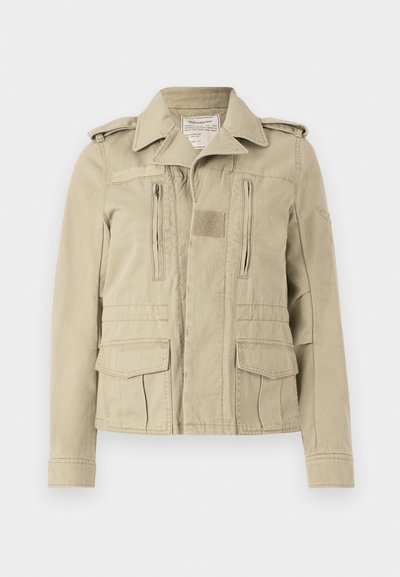 Beige Baumwolljacke im Militärstil mit Knopfverschluss, zwei Reißverschlusstaschen auf der Brust und seitlichen Klappentaschen. Mit Schulterklappen und einem strukturierten Kragen.