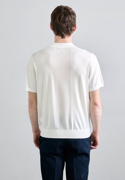 Vit stickad tröja med korta ärmar och texturerat mönster på ryggen, ribbad krage och fåll, slät tygstruktur och figurnära silhuett.