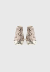 Ett par högstövlar i Converse All Star med beige och svart ormtryck, visade bakifrån på en vit bakgrund.