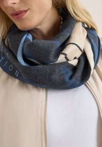 Gestrickter Schal in Grau, Beige und Blau mit abstrakten Mustern. Weiche Textur, geschlungenes Design und glatte Oberfläche. Lässig um den Hals getragen.