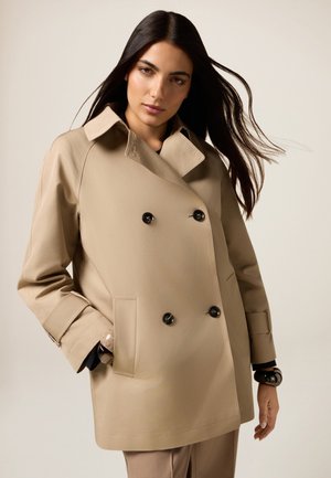 Beige dubbelzijdig trenchcoat met zwarte knopen, grote kraag en klepzakken. Soepele, gestructureerde stof met een getailleerde pasvorm.