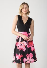 Robe florale noire et rose avec un décolleté en V, sans manches, et une jupe évasée ornée de grandes fleurs roses sur fond noir.