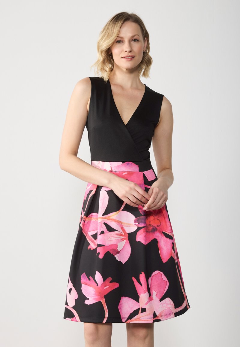 Robe florale noire et rose avec un décolleté en V, sans manches, et une jupe évasée ornée de grandes fleurs roses sur fond noir.