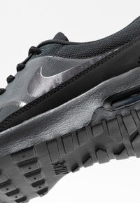 Baskets Nike noires et grises avec une semelle texturée, coussin d'air visible et logo Swoosh réfléchissant sur le côté.