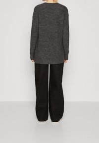 Übergroßer dunkelgrauer Strickpullover mit strukturierter Stoffqualität, langen Ärmeln und geripptem Saum, kombiniert mit lockeren schwarzen Hosen mit dezenten Verzierungen.