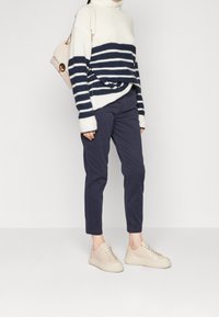 Randig oversized tröja i kräm och marinblått, marinblå byxor, beige sneakers med en slät textur. Stilig väska med axelrem.