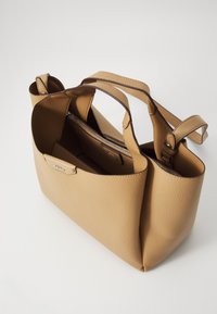 Sac à main en cuir tan avec un design structuré, deux poignées de transport, une poche zippée intérieure et une surface texturée. Base arrondie avec des accents subtils.