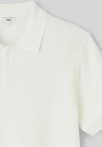Chemise polo blanche en tissu texturé, avec un col classique, trois boutons et des manches courtes. L'étiquette indique "BZB", taille L.
