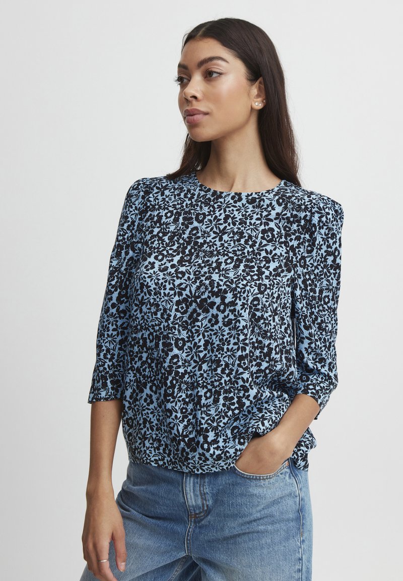 Blusa a fantasia floreale in blu chiaro e nero, con maniche a tre quarti, scollatura rotonda e vestibilità comoda. Tessuto morbido.