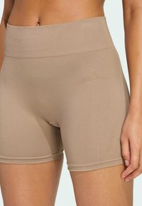 Beige athletic shorts with a wide waistband, made of stretchy fabric. Smooth texture and subtle logo detail on the side.