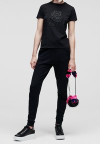 Svart bomull t-shirt med en pärlad grafik, tillsammans med svarta joggers och plattformssneakers. Håller en rosa och svart plyschväska med kedja.