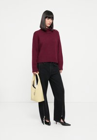 Bordeaux stickad tröja med hög krage, ihop med svarta vida jeans med blixtlåsförsedda detaljer och svarta spetsiga klackskor. Ljust gul handväska.