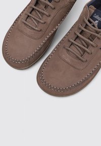 Zapatos de piel marrón con una textura suave, punta redondeada y un pespunte blanco en contraste a lo largo de los bordes. Diseño clásico de cordones.