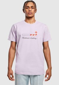 Light purple cotton t-shirt featuring a graphic of a candy cane and text reading "Christmas is loading..." in black. Short sleeves, crew neck.