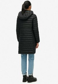 Doudoune noire avec des coutures horizontales, une capuche et un design mi-long. Associée à un jean bleu clair à revers et des bottes noires à lacets.