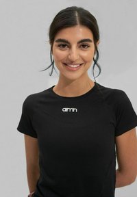 T-shirt de sport noir à manches courtes avec un col rond. Présente un logo blanc sur la poitrine et un tissu lisse et extensible.