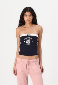 Navy strapless top featuring white accents, front tie detail, and text "NEW YORK CITY 28" with stars. Paired with light pink pants.