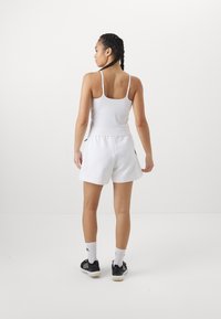 Witte sporttanktop, losse witte shorts, zwarte sportschoenen en witte gestreepte sokken; eenvoudig ontwerp met spaghettibandjes en een gladde textuur.