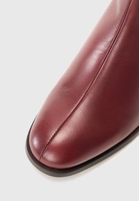 Primo piano della parte anteriore di una scarpa in pelle bordeaux lucida, con una cucitura centrale e suola nera.
