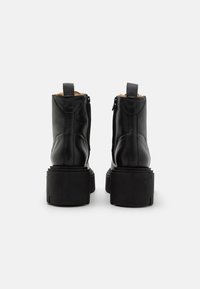 Zwarte leren enkelboots met een gestructureerde afwerking, voorzien van een chunky plateauzool en ritsluiting, verfraaid met een aantreklipje aan de achterkant.