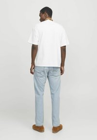Hvit bomull t-skjorte med korte ermer, sammen med lyseblå denimjeans. Brune semskede slip-on-sko og et minimalistisk design.