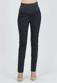 Marinefarbene Umstandshosen mit einem glatten, dehnbaren Taillenbund. Slim-Fit-Design, akzentuiert mit einem subtilen Vorderfalten, kombiniert mit hellgrauen Absätzen.