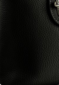 Schwarze Leder-Handtasche mit strukturierter Oberfläche und abgerundeten Kanten, ausgestattet mit einem silbernen Verschluss und einem minimalistischen Design.