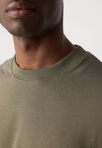 Green cotton t-shirt with a round ribbed neckline. The fabric has a smooth texture and a fitted cut, showing part of the neck.
