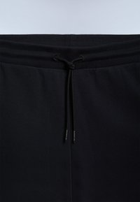 Mustad riidest püksid soonilise elastse vöökohaga ja lipsuga nööriga, mille otstel on väike bränditud tekst.