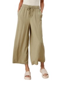 Szerokie spodnie w kolorze jasnej oliwki z elastyczną gumką w pasie, sznurkiem do regulacji i bocznymi kieszeniami, zestawione z beżowymi sandałami wsuwanymi.